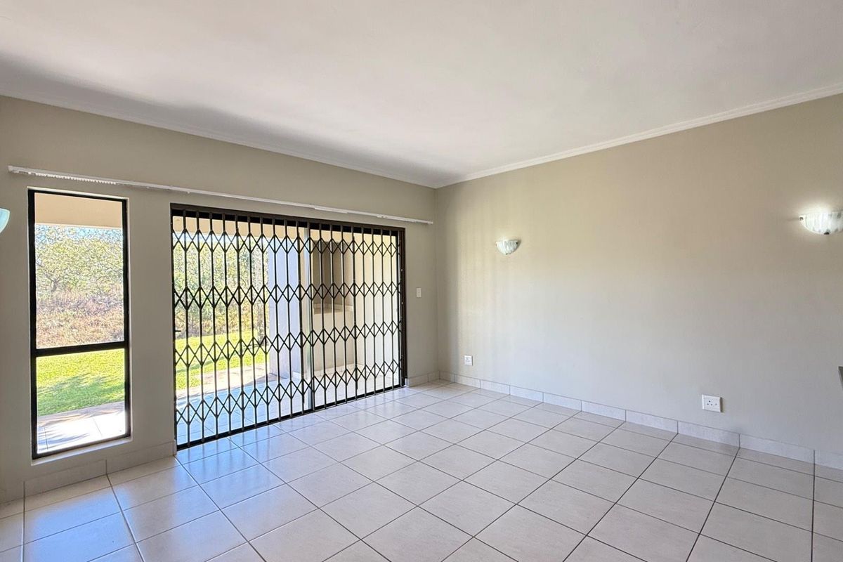 A bright, empty living area featuring neutral tiled floors, wall sconce lighting, and a sliding glass door with a security gate leading outdoors.