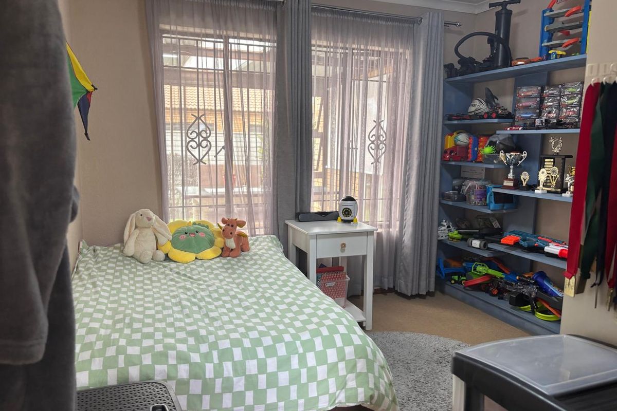 A bedroom featuring built-in shelving and large windows with security bars, providing natural light and functional storage space.