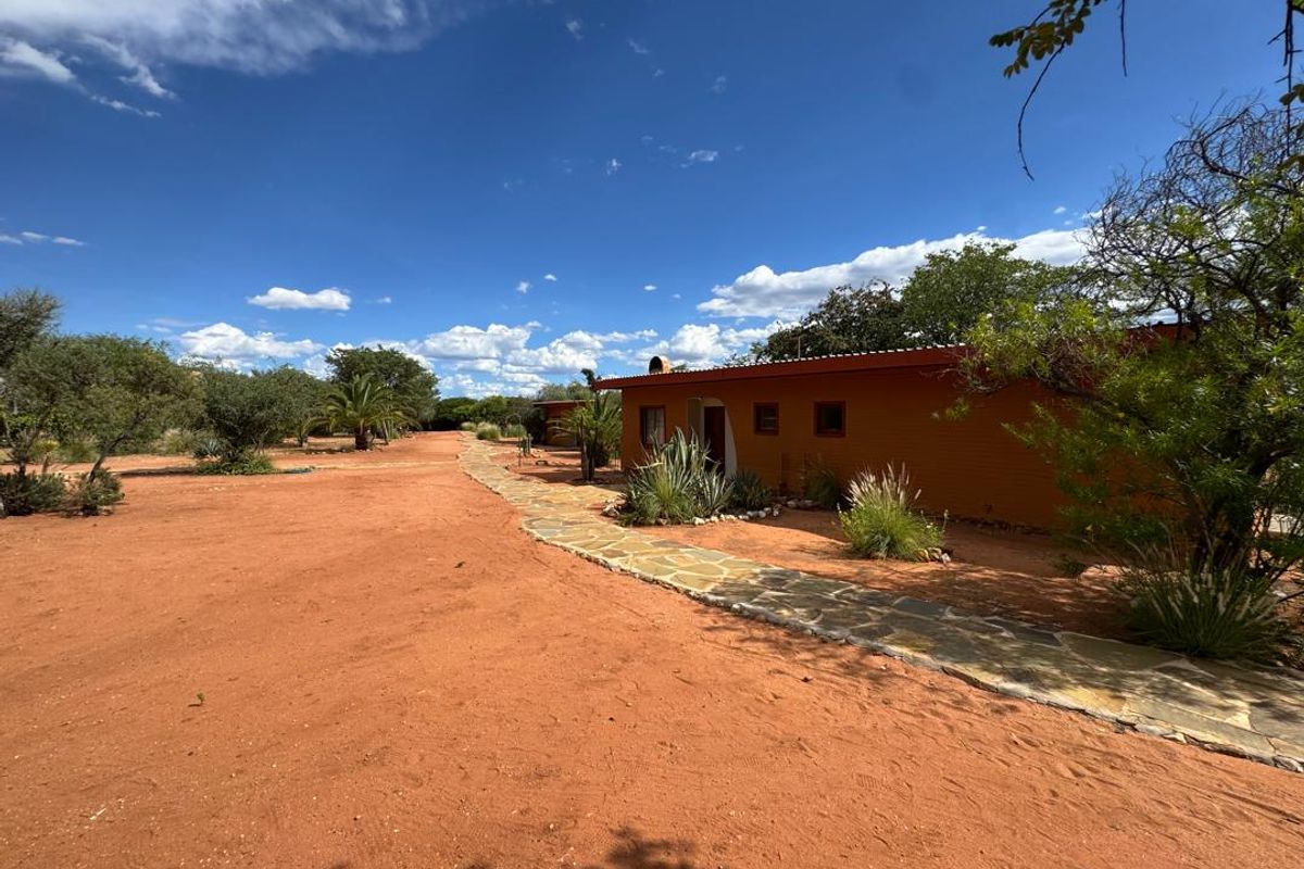 Exterior view of the lodge building featuring a stone pathway leading along the facade, set within a natural, arid landscape.