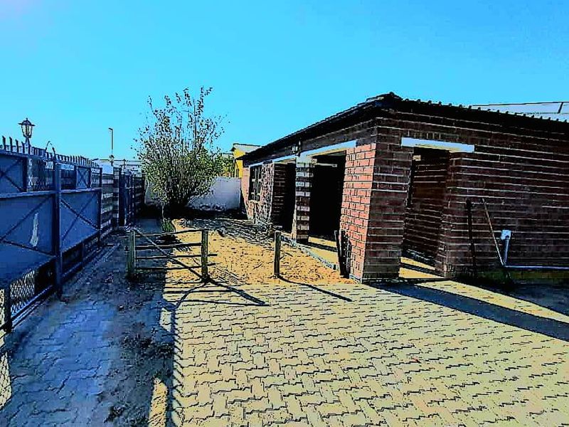 Rear exterior view of a brick house featuring a paved driveway, perimeter fencing, and gated access to the yard area.