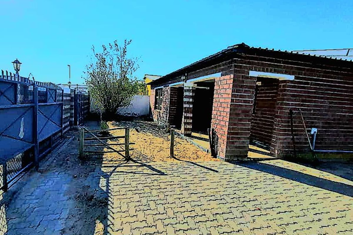 Rear exterior view of a brick house featuring a paved driveway, perimeter fencing, and gated access to the yard area.