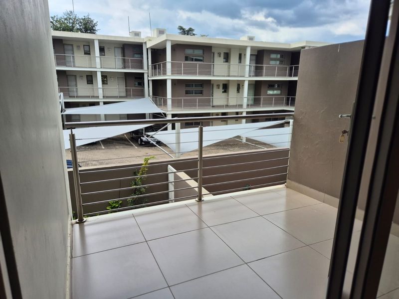 A clean, tiled balcony featuring a modern stainless steel balustrade, overlooking the apartment complex parking area with shade sails.