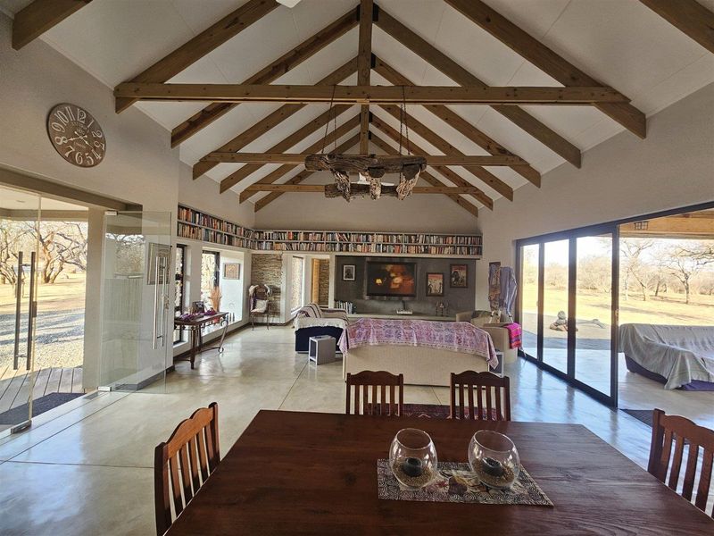 Spacious open-plan living area featuring high vaulted ceilings with exposed timber trusses, polished concrete floors, and expansive sliding glass doors opening to the outdoors.
