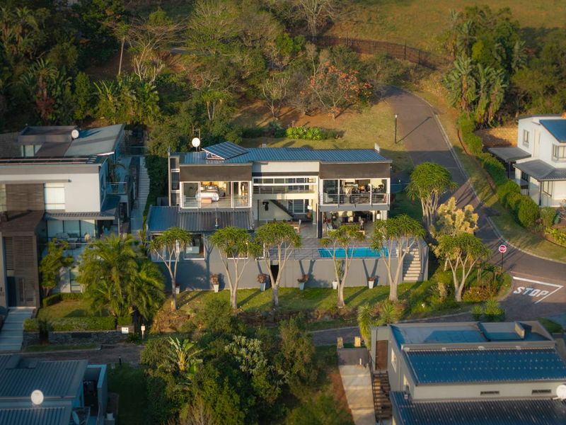 Aerial view of a modern multi-level residential property featuring a swimming pool, balconies, and solar panels set within a landscaped estate environment.
