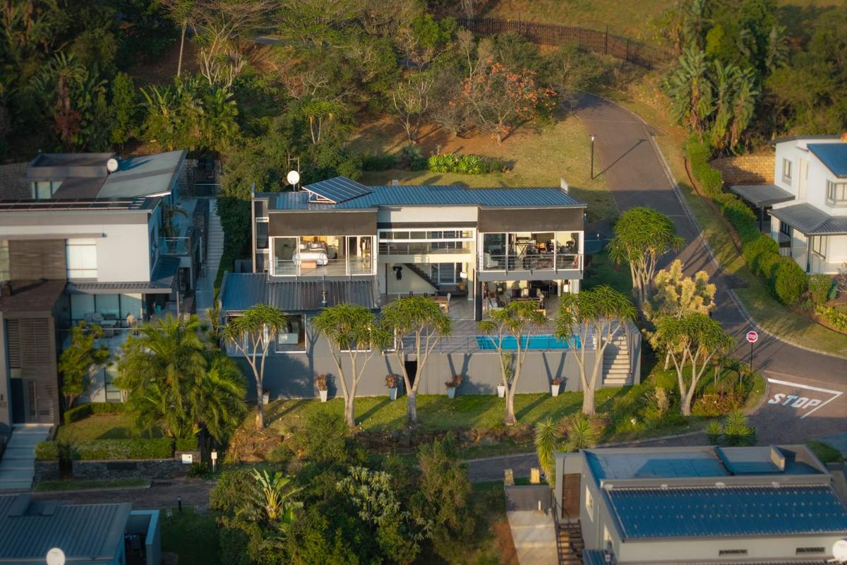 Aerial view of a modern multi-level residential property featuring a swimming pool, balconies, and solar panels set within a landscaped estate environment.
