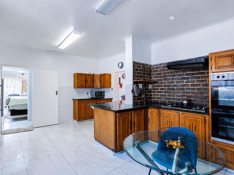 A functional kitchen featuring timber cabinetry, granite countertops, and an exposed brick feature wall, complemented by modern porcelain floor tiles.