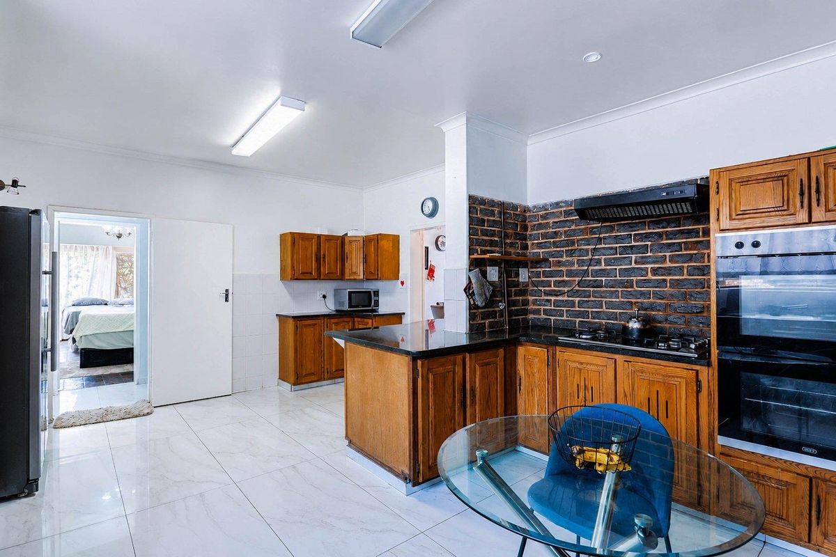 A functional kitchen featuring timber cabinetry, granite countertops, and an exposed brick feature wall, complemented by modern porcelain floor tiles.