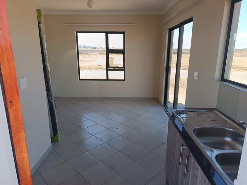 An open-plan living and kitchen area featuring tiled flooring, modern cabinetry with granite countertops, and large windows providing natural light.