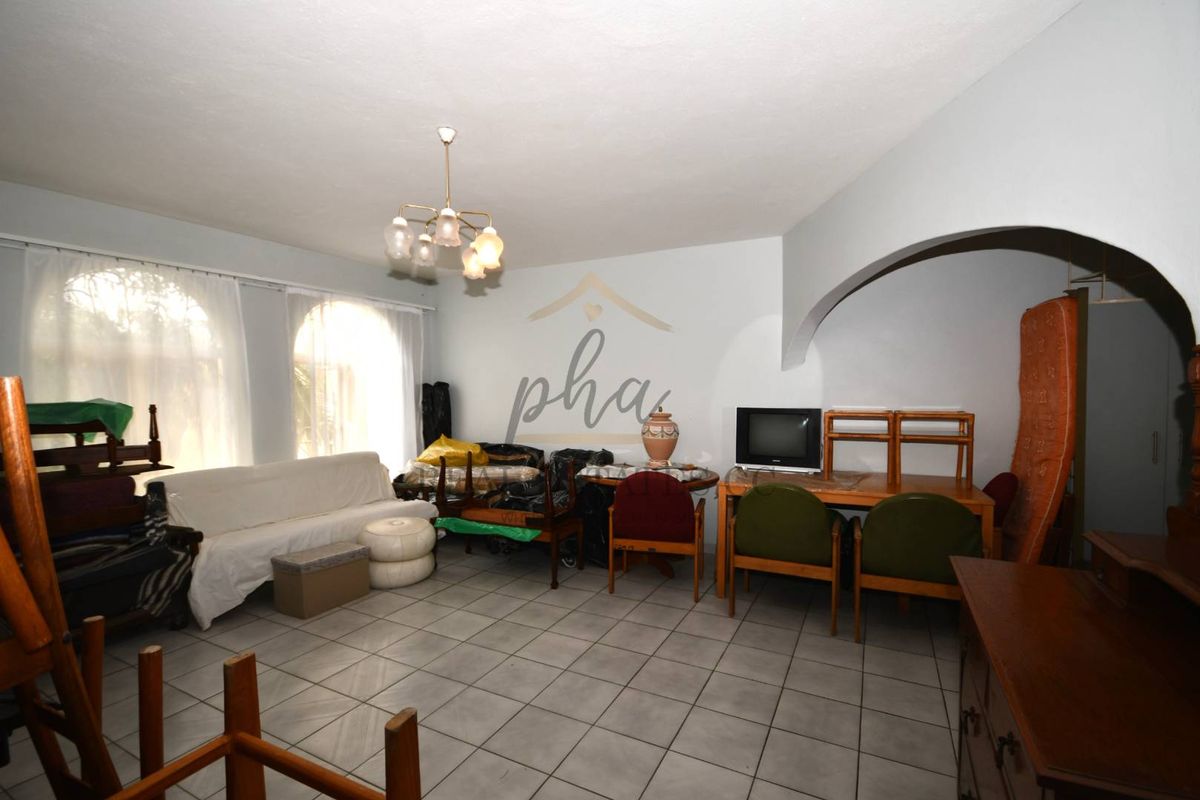 Spacious living area featuring tiled flooring, arched architectural detailing, and large windows allowing for natural light.
