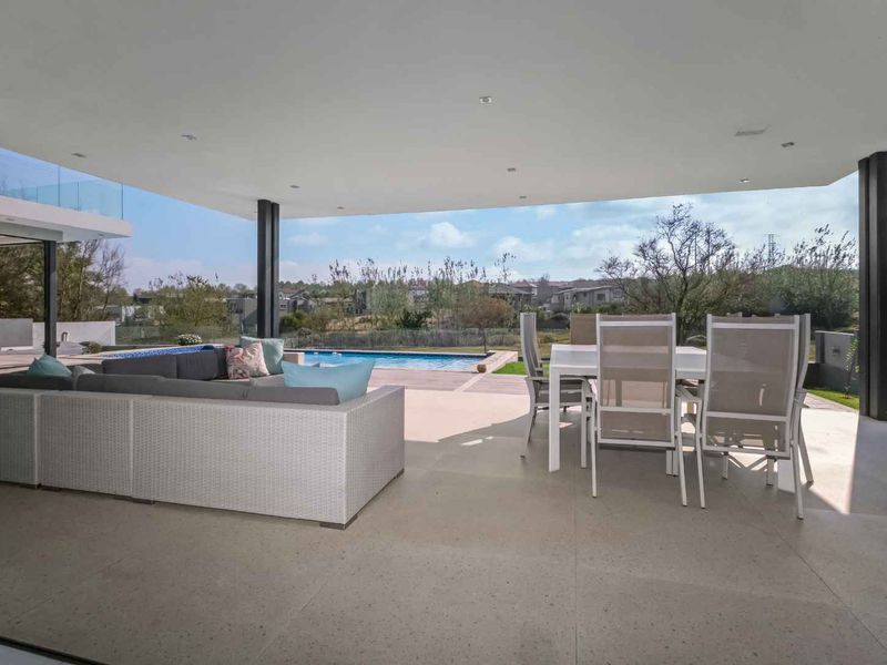 Spacious covered patio featuring stone cladding, recessed lighting, and seamless flow to the outdoor swimming pool and garden area.