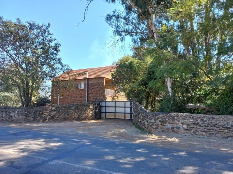 Street view of a facebrick small holding property featuring a stone boundary wall and secure metal entrance gate.