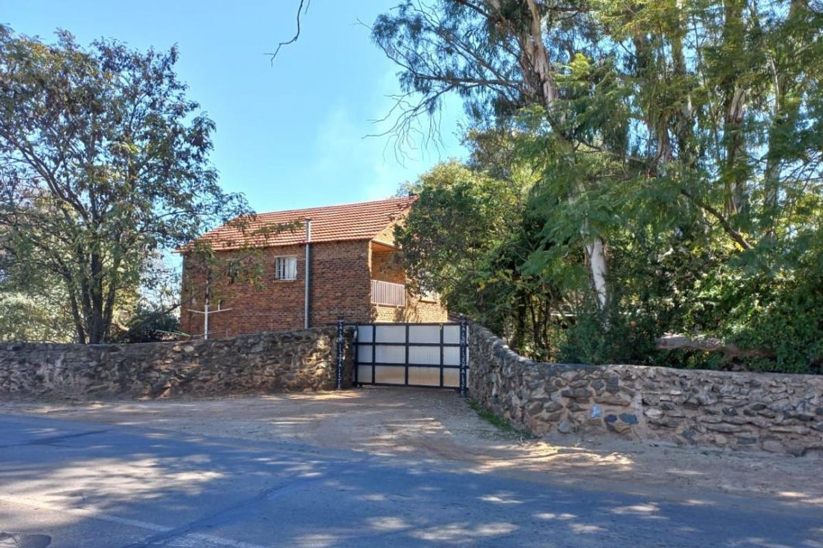 Street view of a facebrick small holding property featuring a stone boundary wall and secure metal entrance gate.
