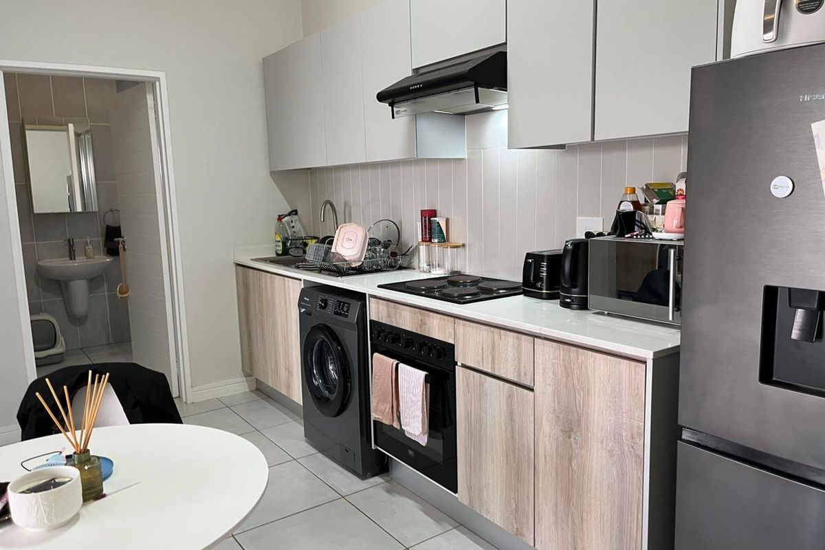 Modern kitchen featuring light wood-grain cabinetry, integrated oven and hob, extractor fan, and tiled backsplash, with an adjacent bathroom visible.