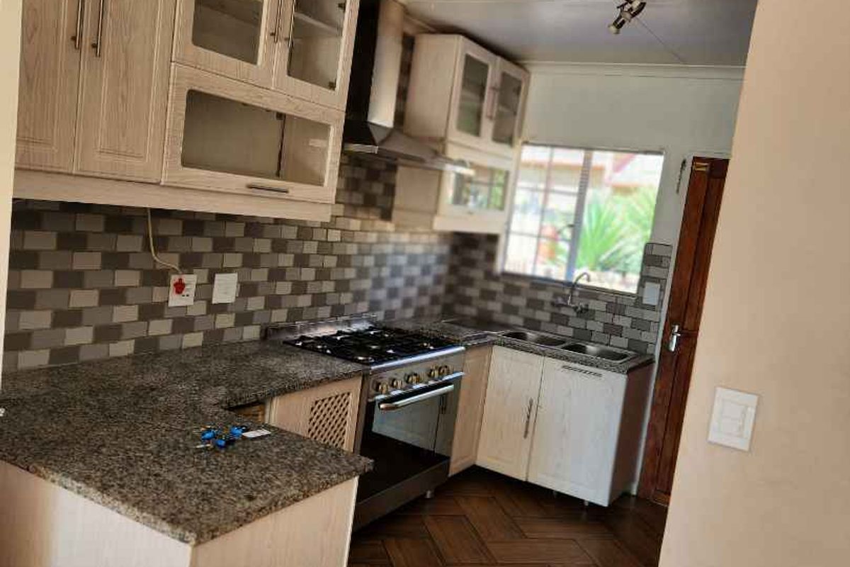 A functional kitchen featuring light wood cabinetry, granite countertops, a gas hob with extractor, and stylish herringbone flooring.