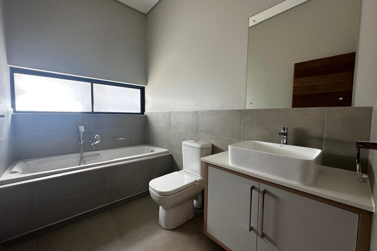Modern bathroom featuring a built-in bathtub, a contemporary vessel sink vanity, a wall-mounted mirror, and neutral floor-to-ceiling tiling.