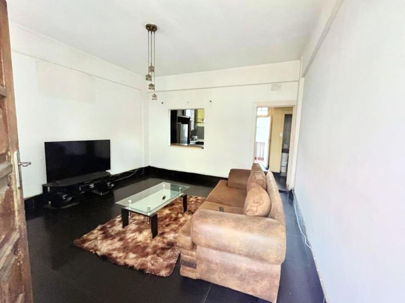 A living room featuring dark tiled flooring, a serving hatch connecting to the kitchen, and a central pendant light fixture.