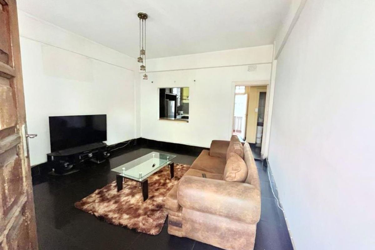 A living room featuring dark tiled flooring, a serving hatch connecting to the kitchen, and a central pendant light fixture.