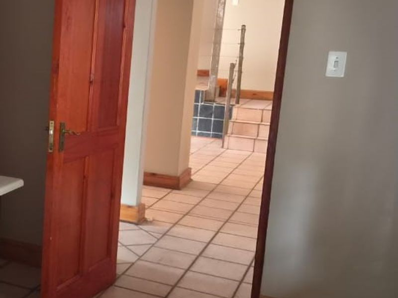 A view through a wooden door into a tiled hallway leading to a staircase, featuring neutral wall tones and classic architectural detailing.