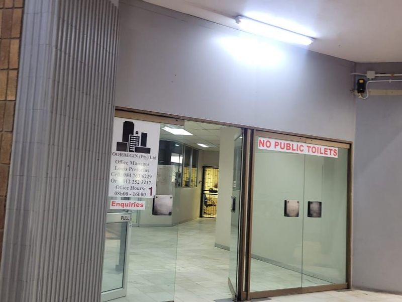 Entrance area to a commercial office space featuring glass double doors, tiled flooring, and overhead fluorescent lighting.