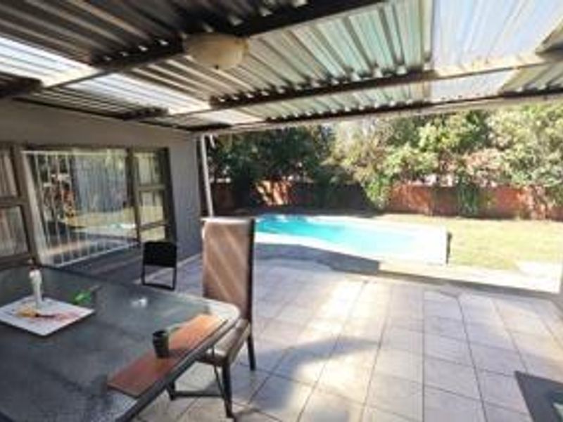 Covered outdoor patio area featuring tiled flooring and a corrugated roof, overlooking a private swimming pool and garden space.