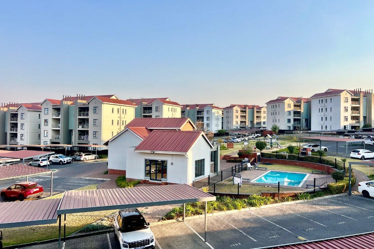 Aerial view of a residential apartment complex featuring multiple buildings, a communal swimming pool, and covered parking bays.