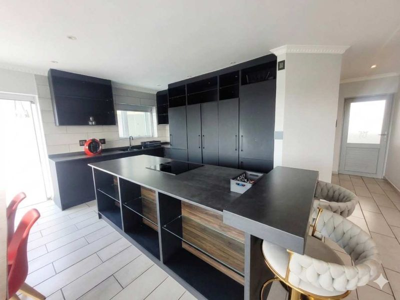 Modern kitchen featuring dark cabinetry, a large central island with a built-in hob, and tiled flooring, offering a sleek and functional cooking space.