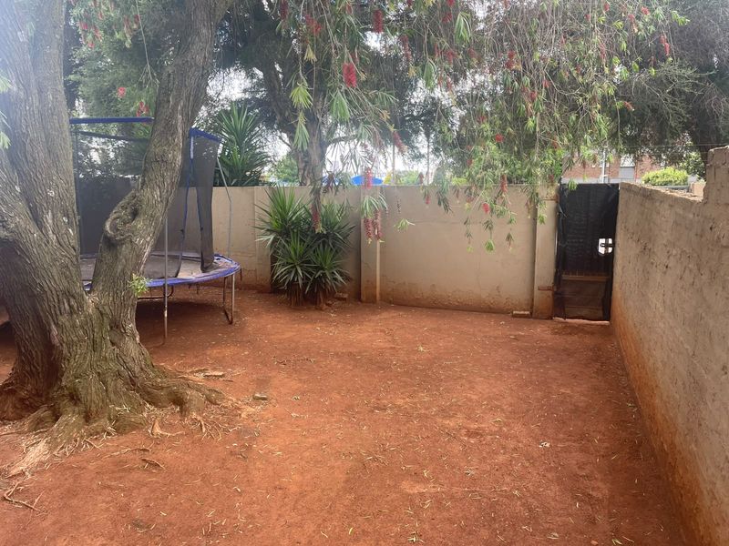 A private rear courtyard area featuring a perimeter boundary wall, access gate, and mature tree, offering potential for landscaping and outdoor improvement.