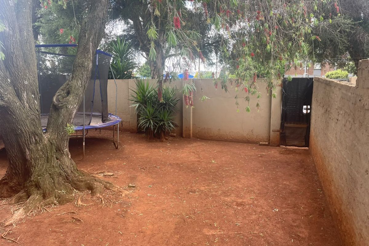 A private rear courtyard area featuring a perimeter boundary wall, access gate, and mature tree, offering potential for landscaping and outdoor improvement.