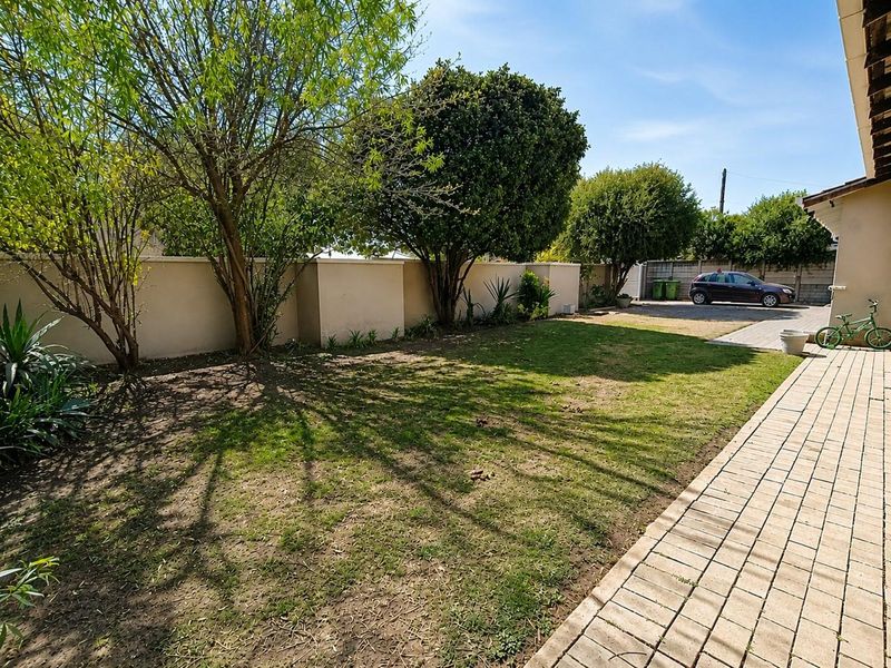 A rear garden area featuring a paved walkway, boundary wall, and established trees with a lawn space.
