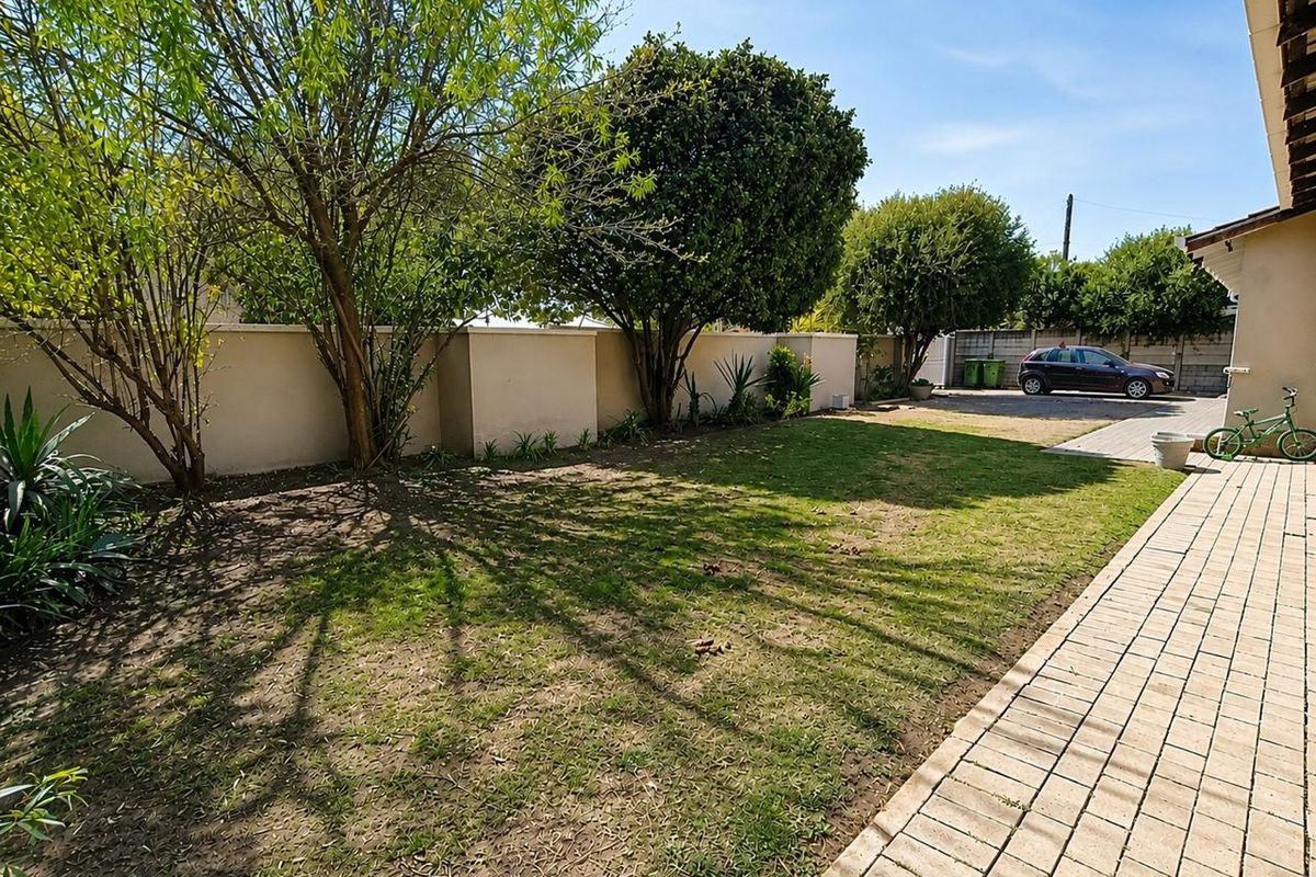 A rear garden area featuring a paved walkway, boundary wall, and established trees with a lawn space.