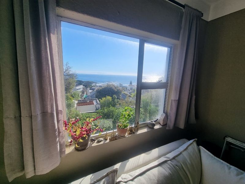 A bright room featuring a large window with a scenic coastal and ocean view, showcasing natural light and established greenery.