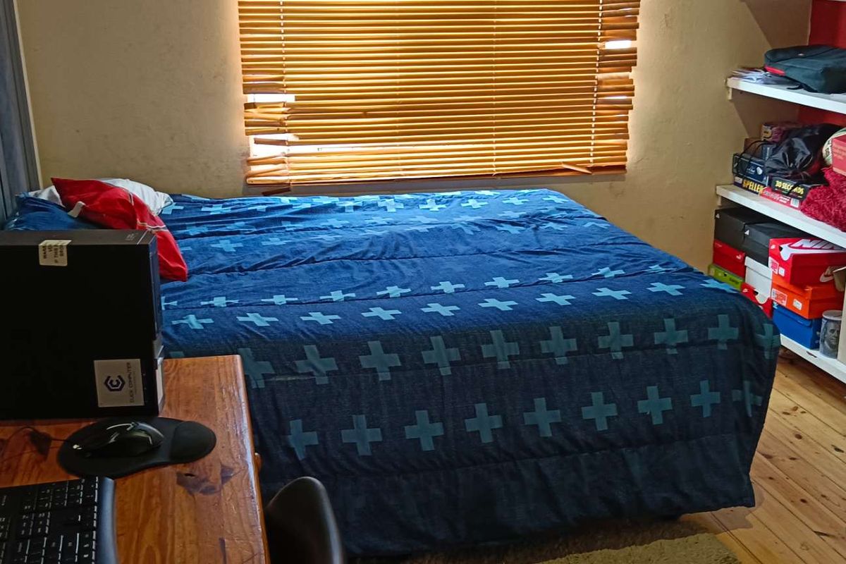 A functional bedroom featuring timber flooring, built-in shelving units, and venetian blinds.