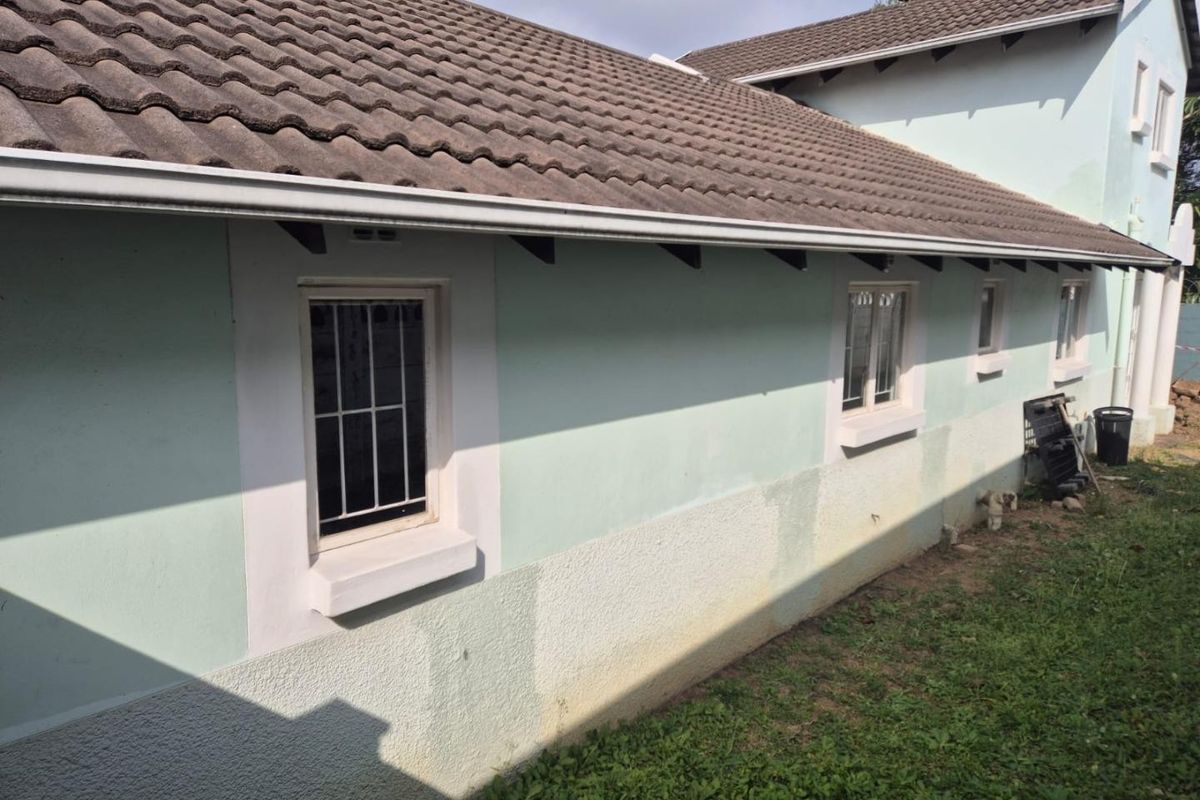 Rear exterior view of the townhouse featuring concrete roof tiles, white-framed windows with security bars, and plastered walls showing signs of weathering.