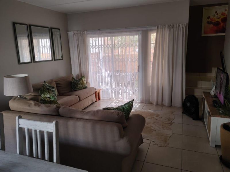 A comfortable living room featuring tiled flooring and a large sliding glass door with a security gate, providing access to the outdoor area.