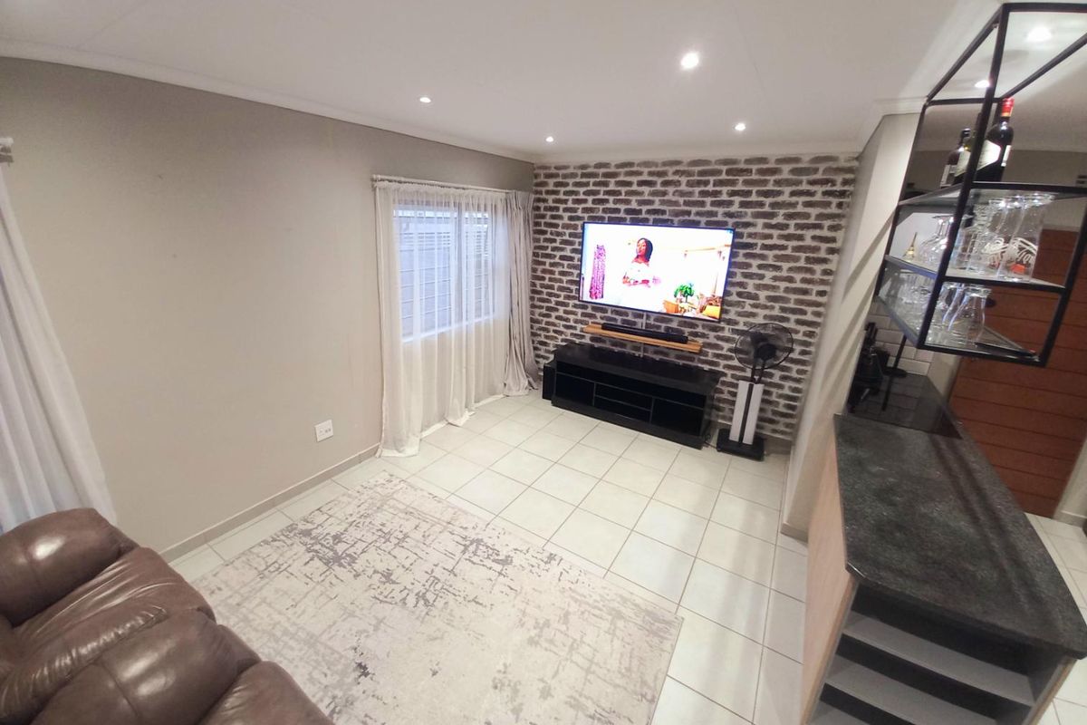 A modern living room featuring a distinctive exposed brick feature wall, tiled flooring, and recessed ceiling lighting.
