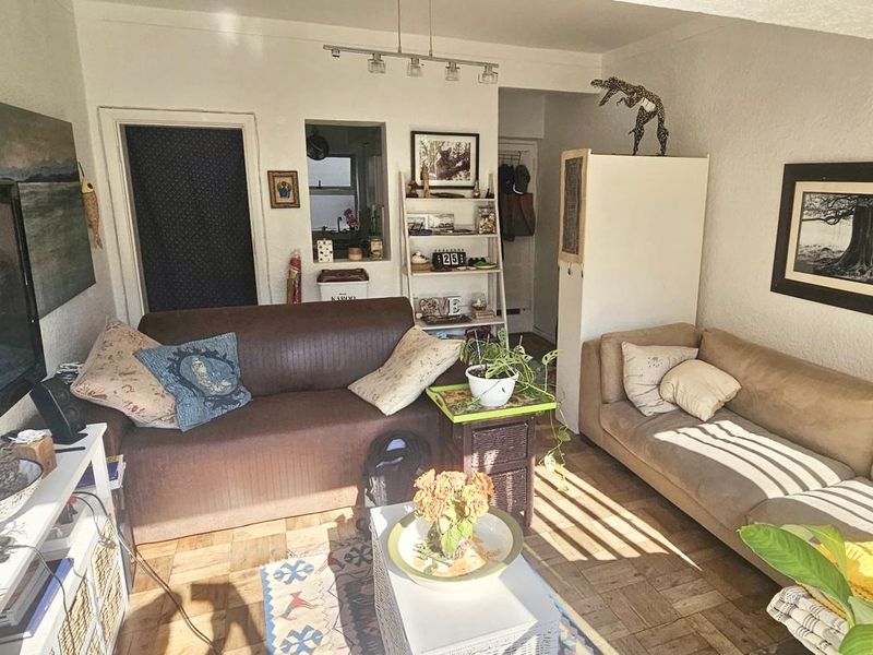 A cozy living room featuring classic parquet flooring, a convenient pass-through window to the kitchen area, and modern track lighting.