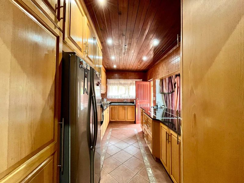 A galley-style kitchen featuring extensive wooden cabinetry, granite countertops, a double sink, and a distinctive wooden tongue and groove ceiling with recessed lighting.