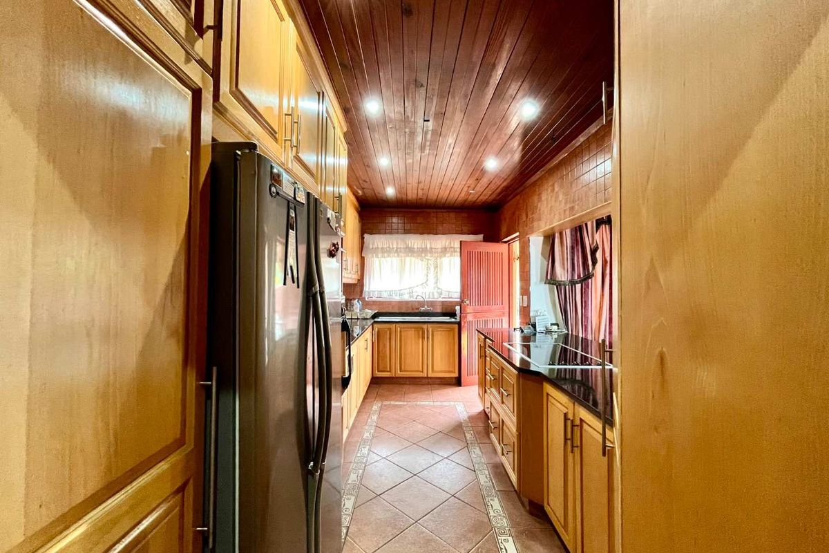 A galley-style kitchen featuring extensive wooden cabinetry, granite countertops, a double sink, and a distinctive wooden tongue and groove ceiling with recessed lighting.