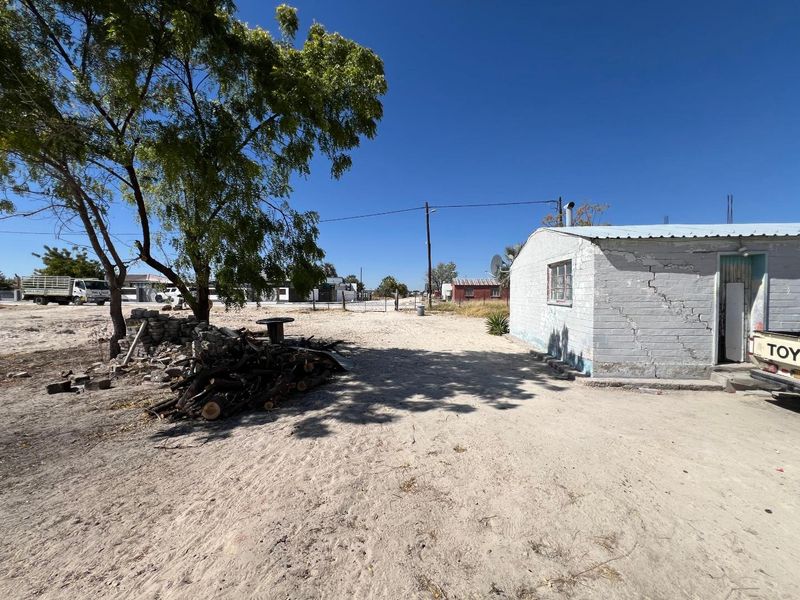 Rear view of a single-story residential structure showing significant structural wall cracking and weathered exterior finishes on a sandy plot.