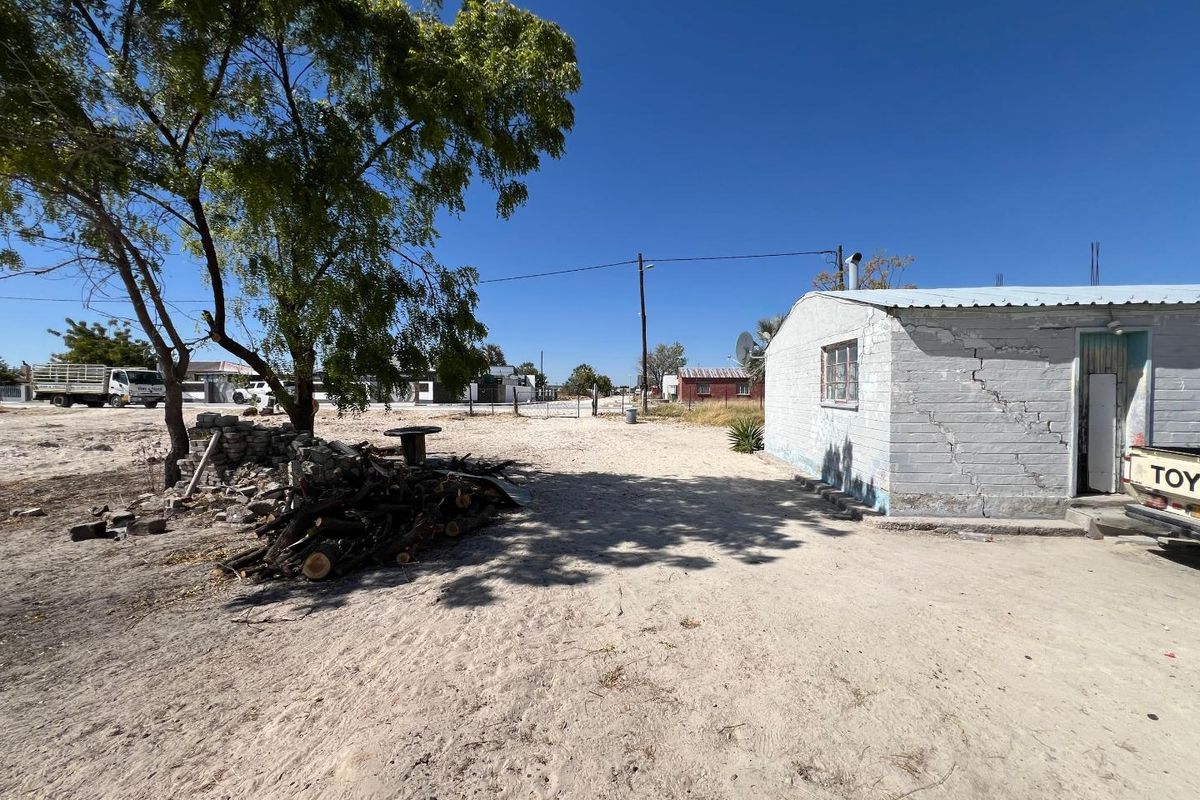 Rear view of a single-story residential structure showing significant structural wall cracking and weathered exterior finishes on a sandy plot.