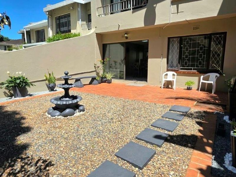 A private rear courtyard featuring a paved patio area, gravel landscaping with stone stepping stones, and secure access to the apartment interior.