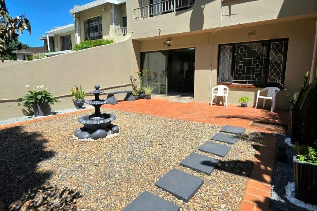 A private rear courtyard featuring a paved patio area, gravel landscaping with stone stepping stones, and secure access to the apartment interior.