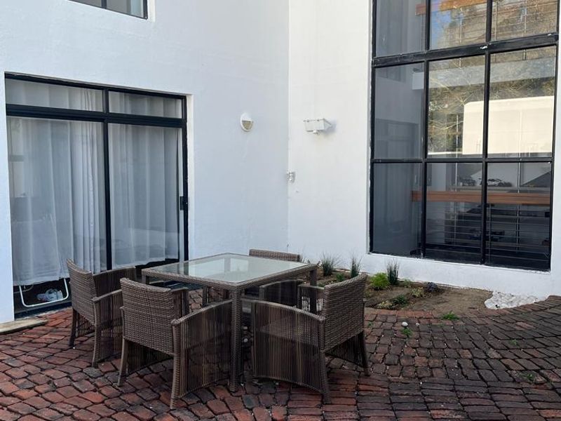 A private courtyard patio featuring traditional brick paving, large floor-to-ceiling windows, and a sliding door entrance, offering a quiet outdoor space.