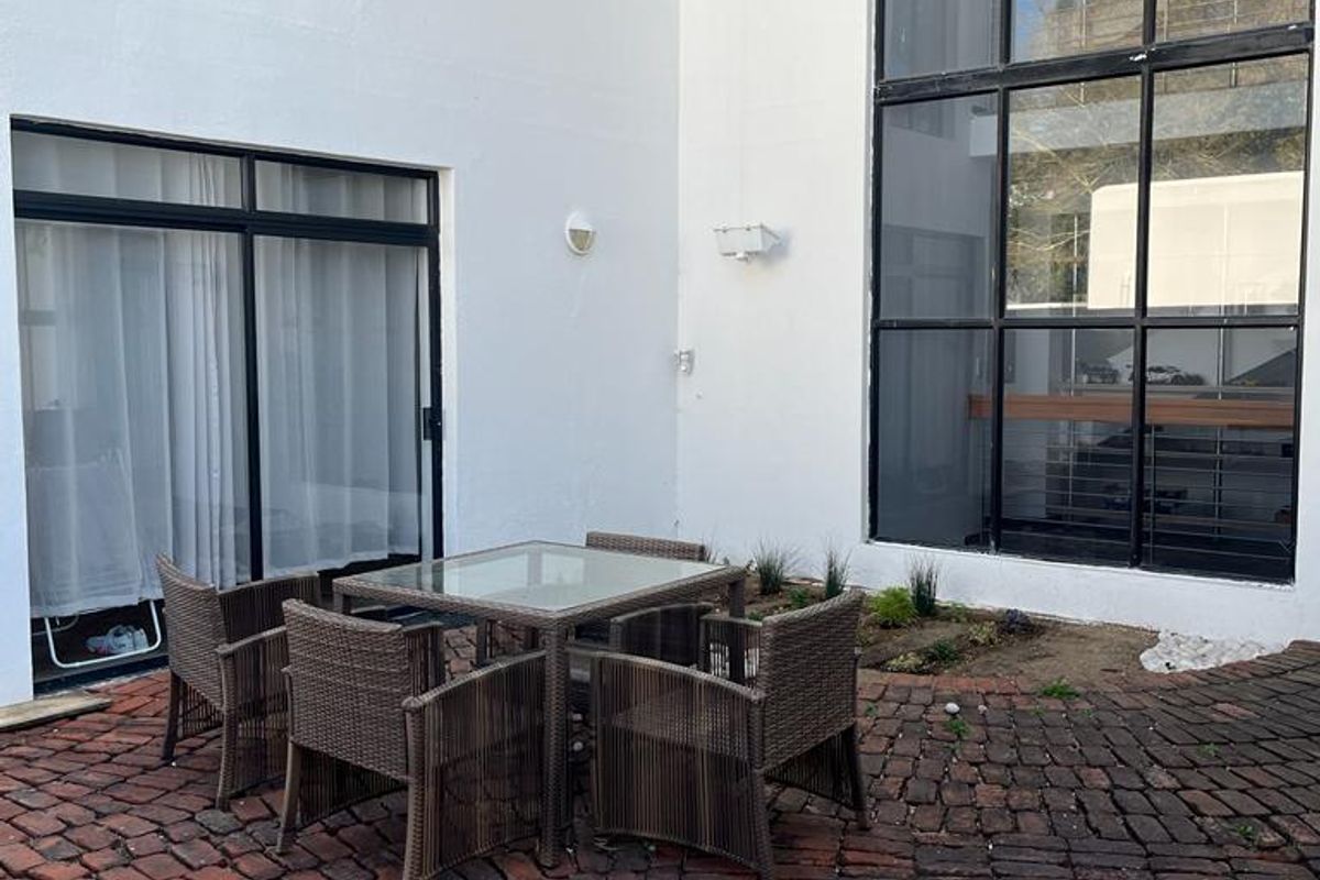 A private courtyard patio featuring traditional brick paving, large floor-to-ceiling windows, and a sliding door entrance, offering a quiet outdoor space.