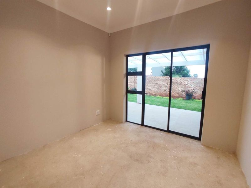An empty bedroom featuring a large sliding glass door that opens onto a patio and garden area, with recessed lighting and unfinished flooring.