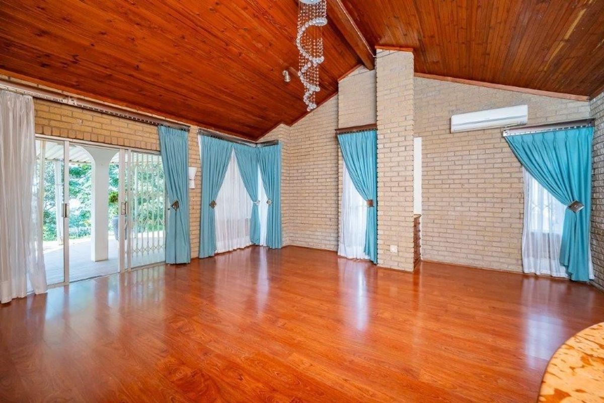 Spacious living area featuring high raked timber ceilings, face brick walls, hardwood flooring, and direct access to an outdoor patio through sliding glass doors.