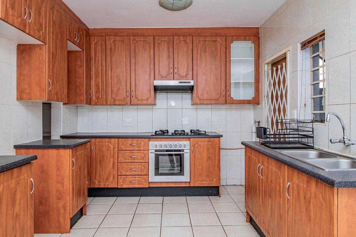 A functional kitchen featuring wood-finish cabinetry, dark laminate countertops, a built-in oven with gas hob, extractor fan, and double stainless steel sink.