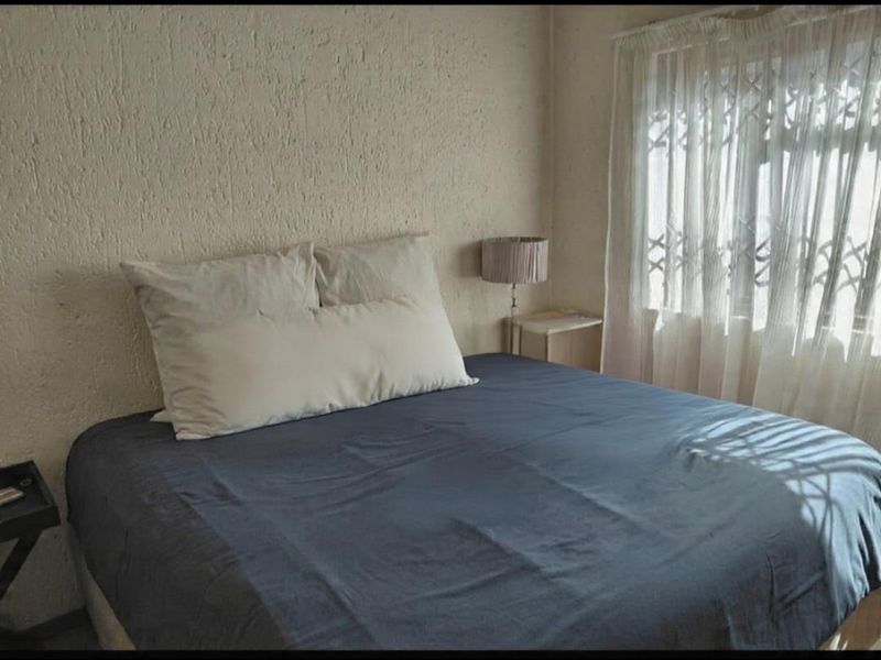 A bedroom featuring textured wall finishes and a window fitted with a security gate.