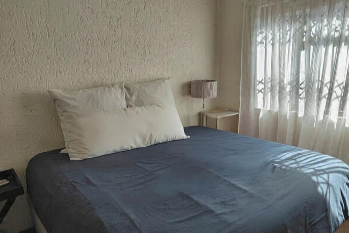 A bedroom featuring textured wall finishes and a window fitted with a security gate.