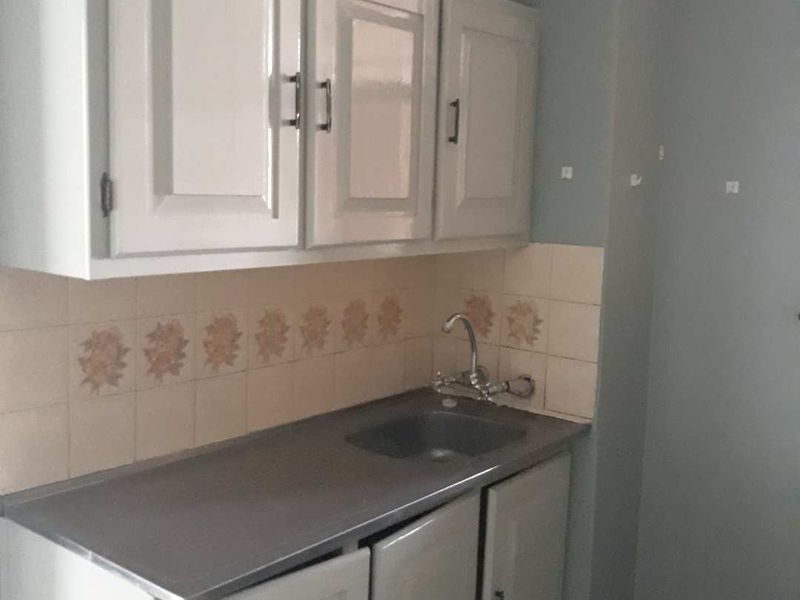 A compact kitchen area featuring basic built-in cabinetry, a stainless steel sink, and a tiled backsplash, currently in need of cosmetic updates.